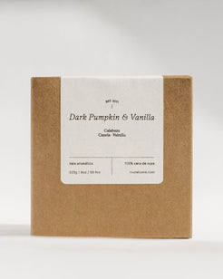 A square kraft paper box with a white paper label reading 'Dark Pumpkin & Vanilla' and smaller text below, photographed on a clean light gray studio background.