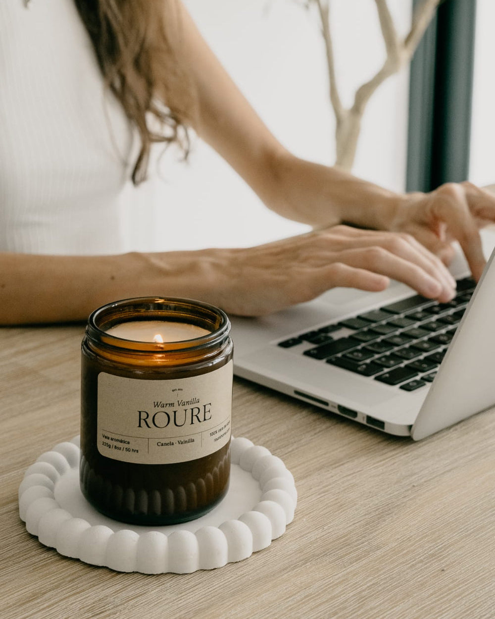 Person using a laptop with a ROURÈ candle on a coaster.