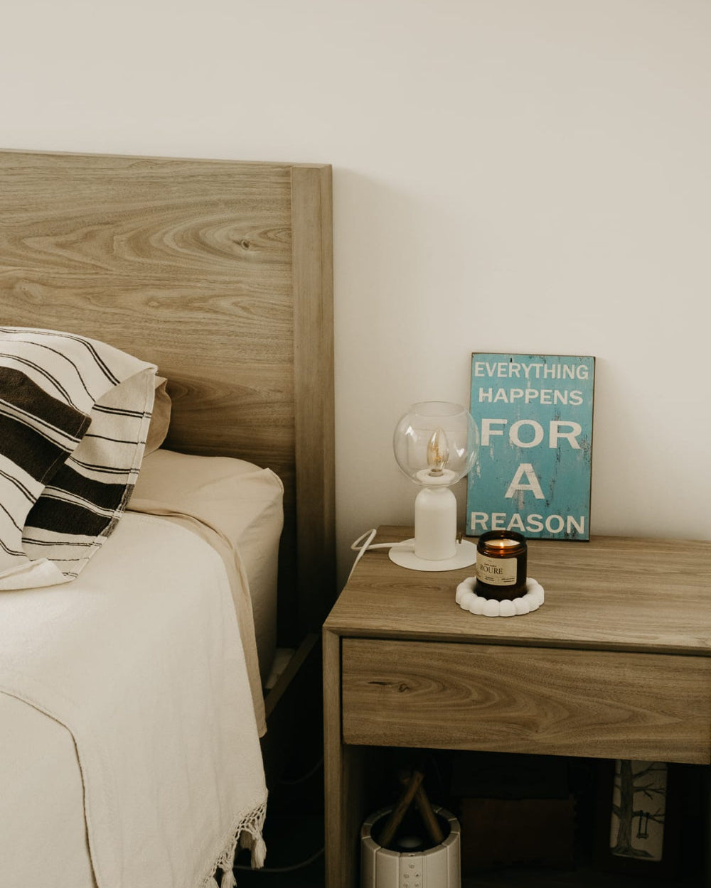 Bedroom with wooden headboard and nightstand, featuring a lamp, candle, and motivational poster.