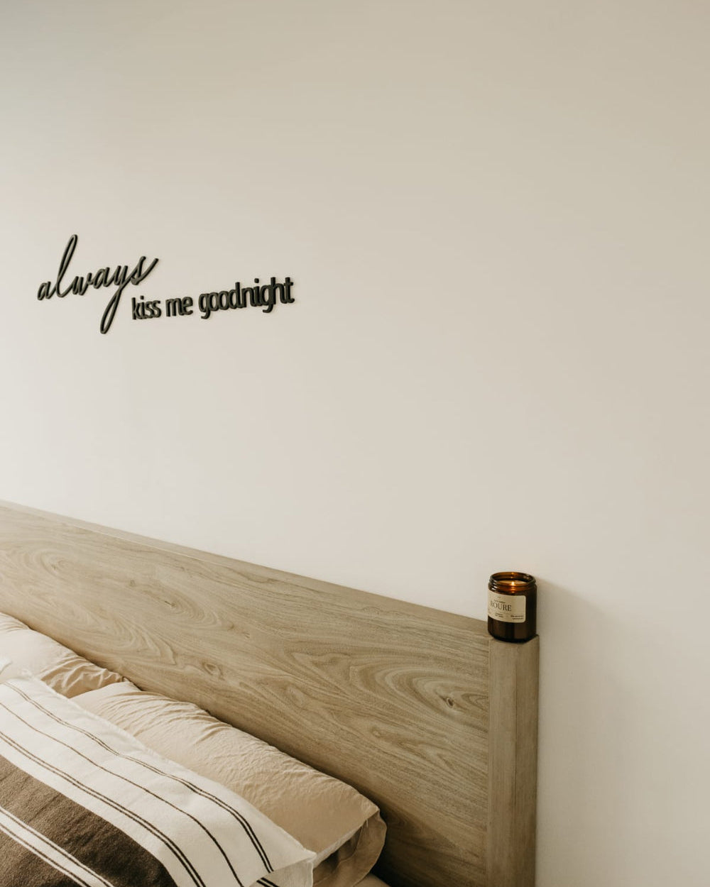 Wooden headboard with 'always kiss me goodnight' wall decal on a neutral wall.