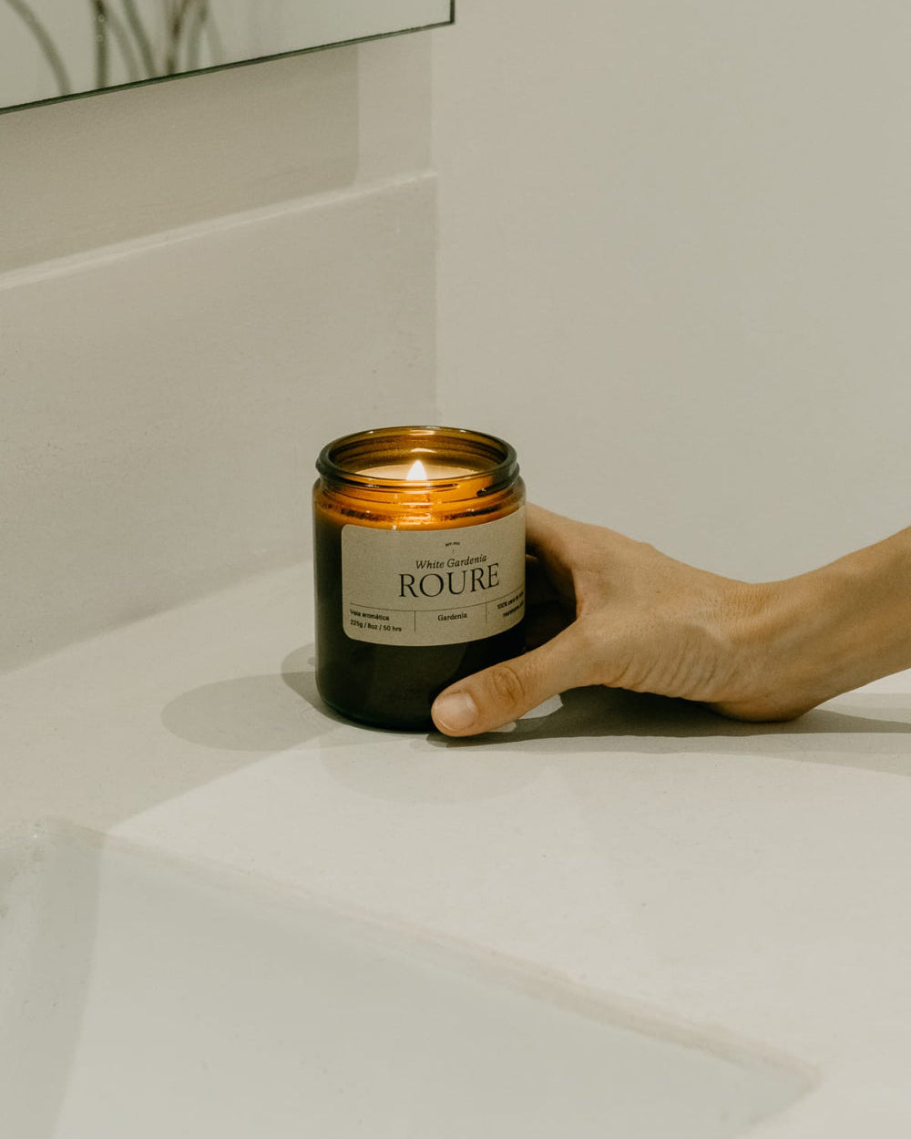 Hand holding a candle labeled 'Roure' on a white surface