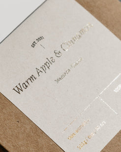 A close-up of a kraft paper box with a cream paper label featuring elegant black serif text and subtle gold foil details.